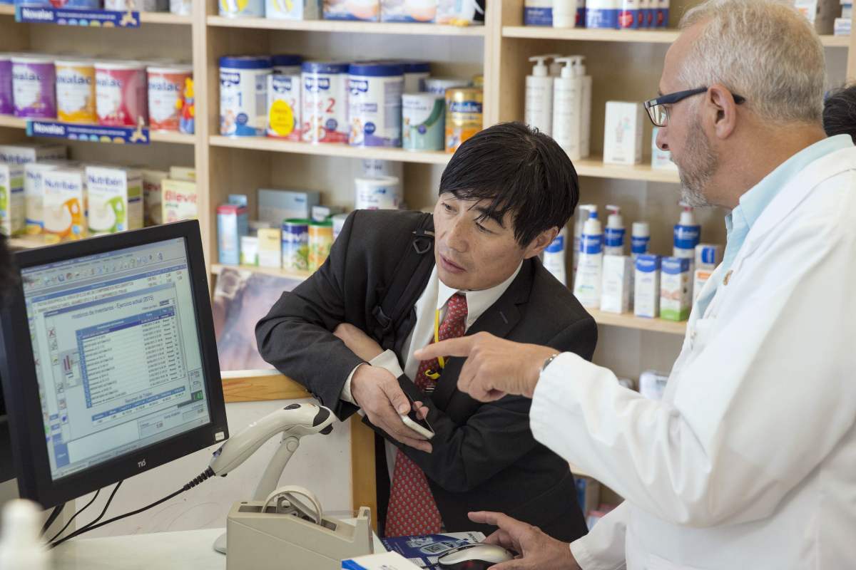 En su farmacia de Sevilla, Manuel Ojeda enseñando a un japonés cómo funciona la receta electrónica, en 2015..