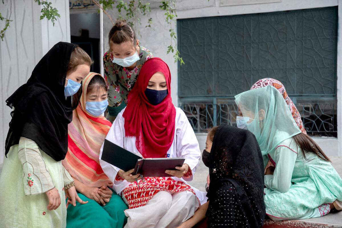 Rodeada de niñas refugiadas, Saleema Rehman les explica cómo ha llegado a convertirse en médico, mostrándoles un álbum fotográfico. /Acnur.