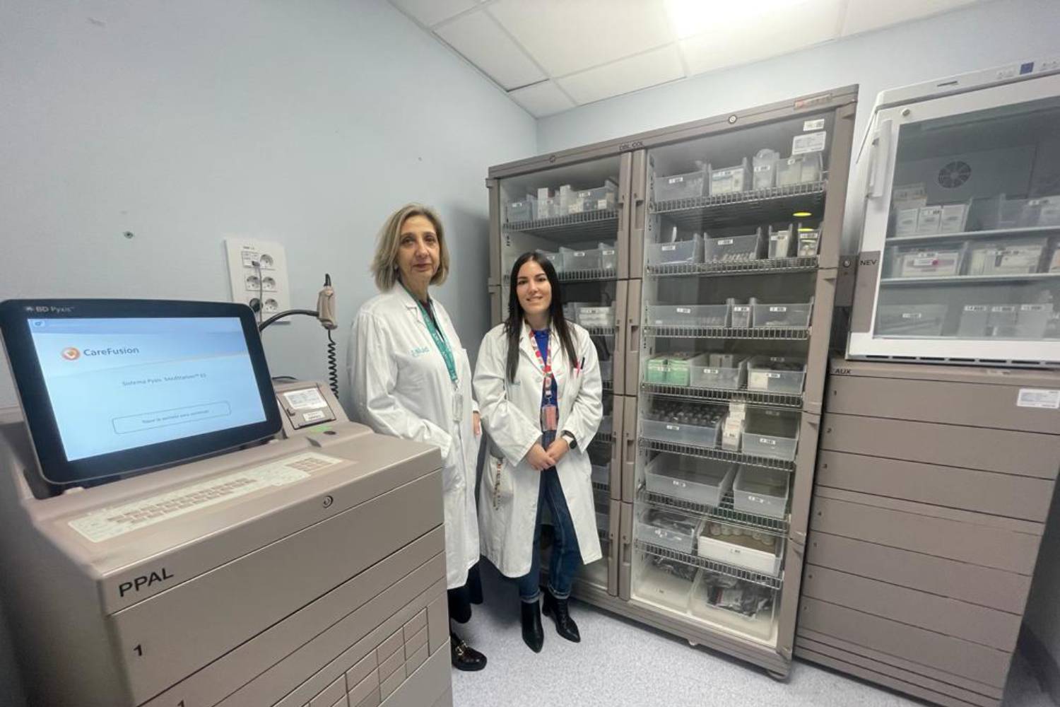Reyes Abad y Pilar Olier, del Servicio de Farmacia del Hospital Miguel Servet, de Zaragoza, posan junto al SAD ubicado en el Servicio de Cirugía Vascular. Foto: HOSPITAL MIGUEL SERVET. 