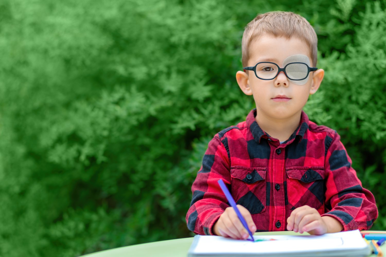 Un niño dibujando, con gafas y un parche. Foto: SHUTTERSTOCK. 