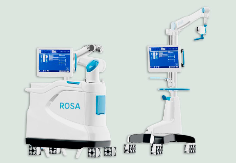 Robot quirúrgico ROSA blanco con pantallas azules y brazo robótico móvil.