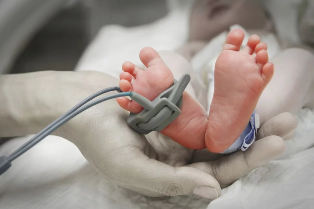 Una madre sostiene los pies de su bebé prematuro en la incubadora.