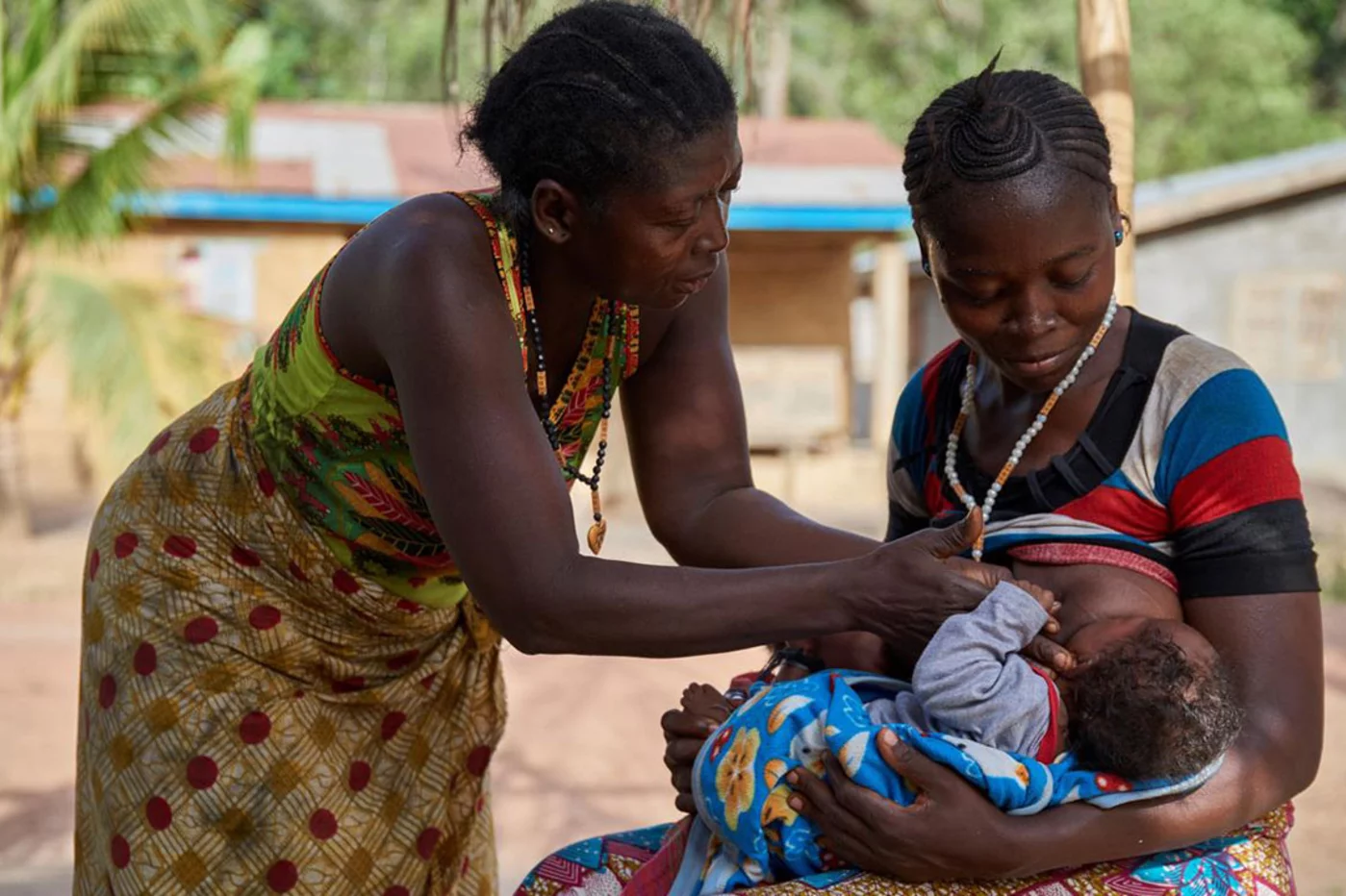 Una madre, ayudada a su vez por su madre, alimenta a uno de sus hijos gemelos de tres meses, en Sierra Leona. El agente de salud comunitario que trabaja en su pueblo es uno de los cerca de 15.000 que se encargan de acercar servicios de salud a sus comunidades.