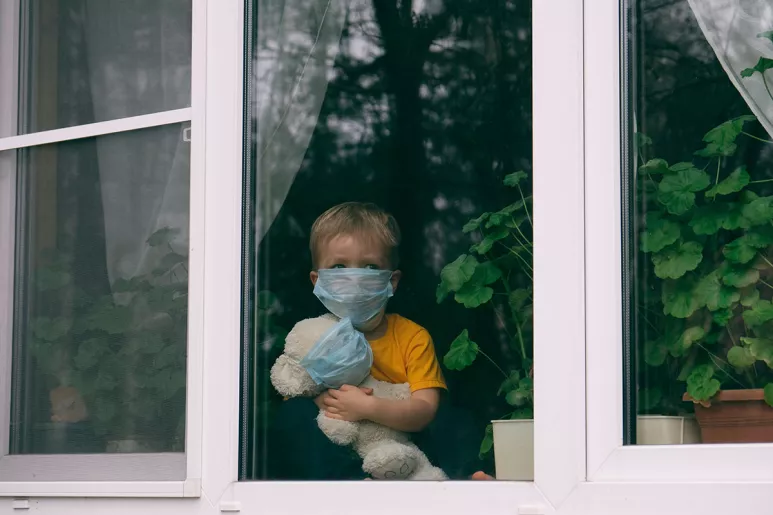 Un niño protegido con una mascarilla mira a través de una ventana.