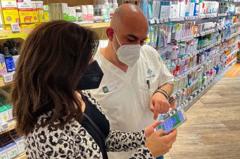 Nacho Mir, farmacéutico comunitario en Barcelona, ofrece el servicio de telemedicina de Alphega. En la imagen, le está explicando el funcionamiento a una usuaria. Foto: ALPHEGA.