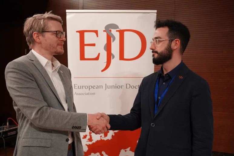 El alemán Mathias Körner y el español Ávaro Cerame, presidente saliente y entrante (respectivamente) de la European Junior Doctors, dándose la mano. Foto: CGCOM.